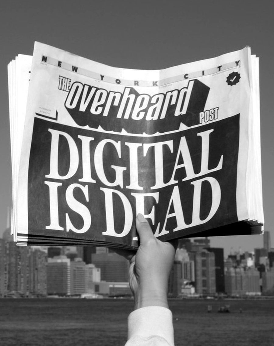 A hand holding up a newspaper headlined 'Digital is Dead' against the New York skyline